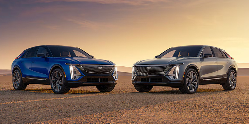 A blue and a gray Cadillac Lyriq electric SUVs parked side by side in a desert landscape at sunset, showcasing their sleek, modern designs and luxury features.