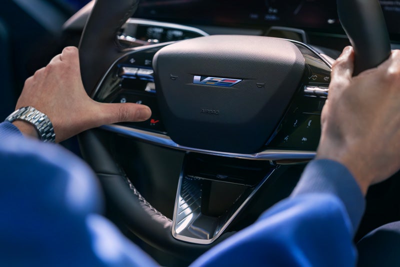 Close-up of a Man About to Press the V-Button on the 2026 OPTIQ-V Steering Wheel | Medina Cadillac in MEDINA OH